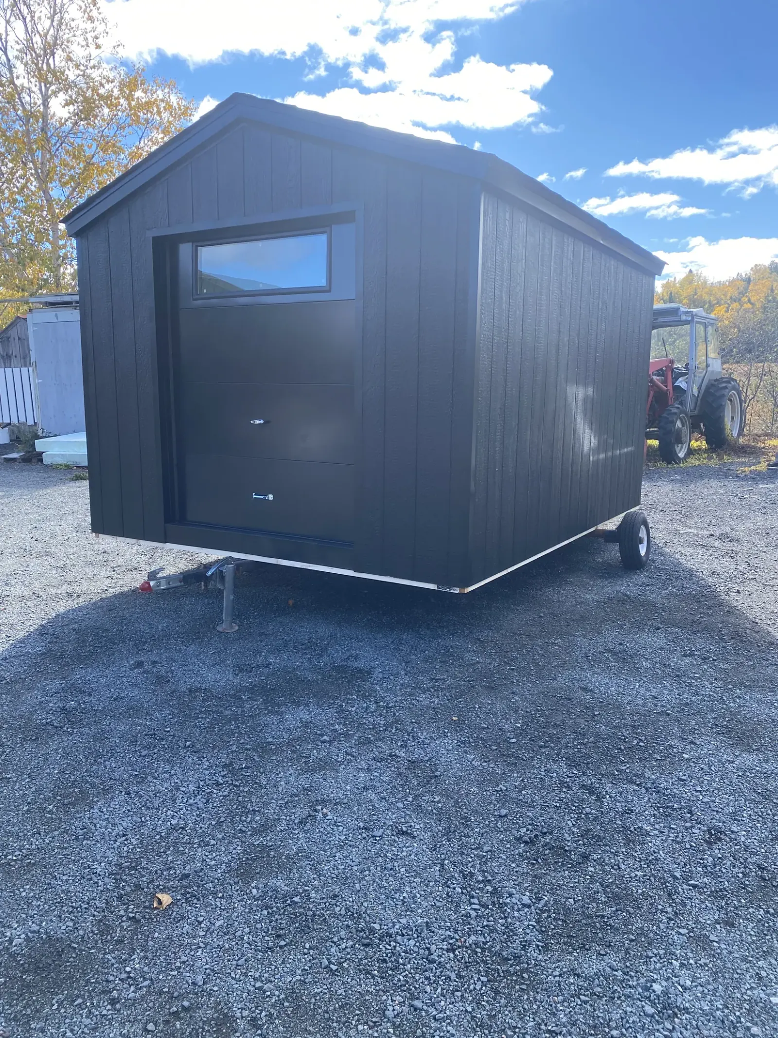 Charcoal-clad building with an angled roofline and a high horizontal window, loaded on a trailer on a gravel yard ready to be delivered
