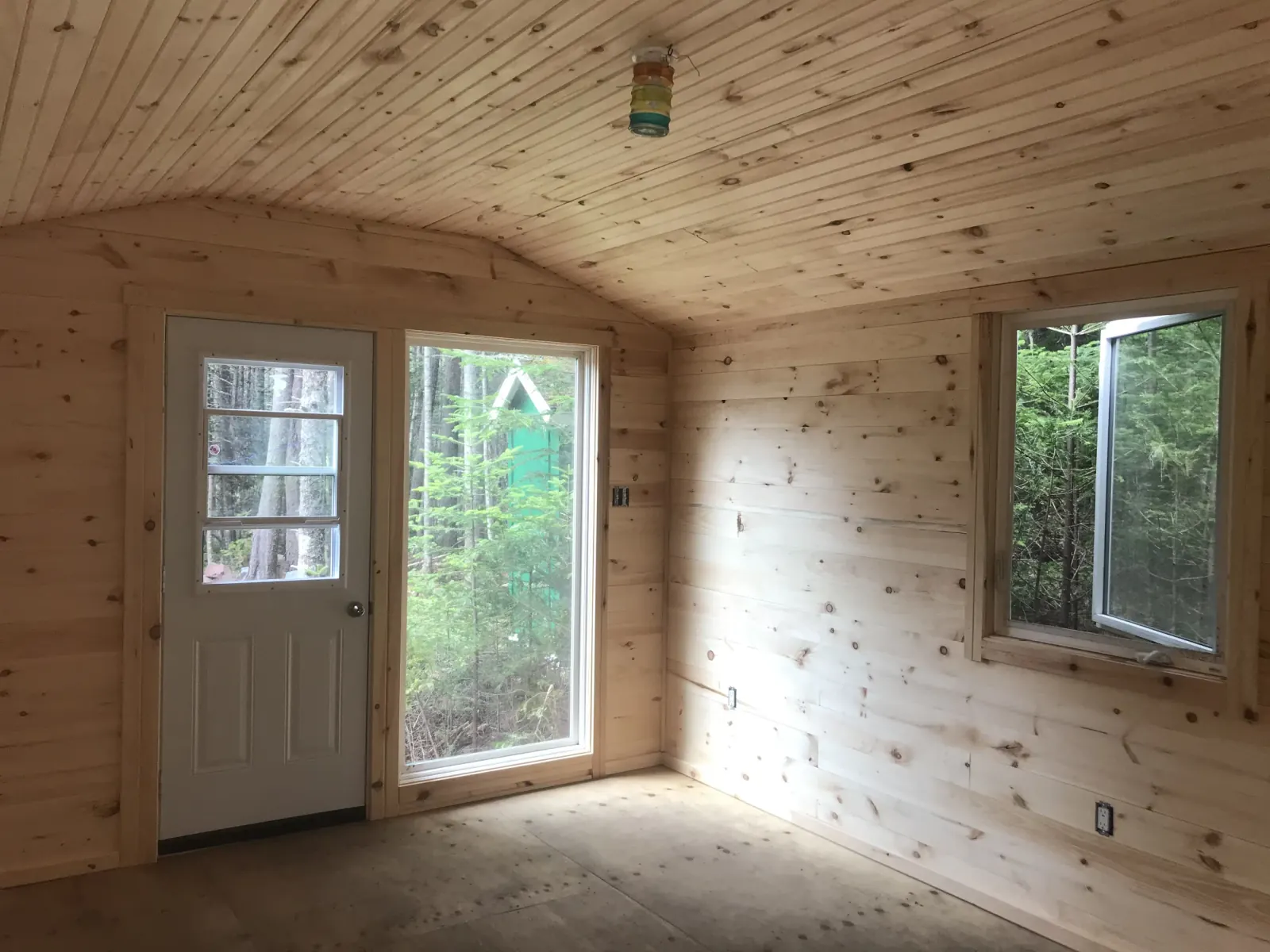 Finished interior lined in knotty pine with a curved boarded ceiling, a glazed entry door and windows looking out to trees