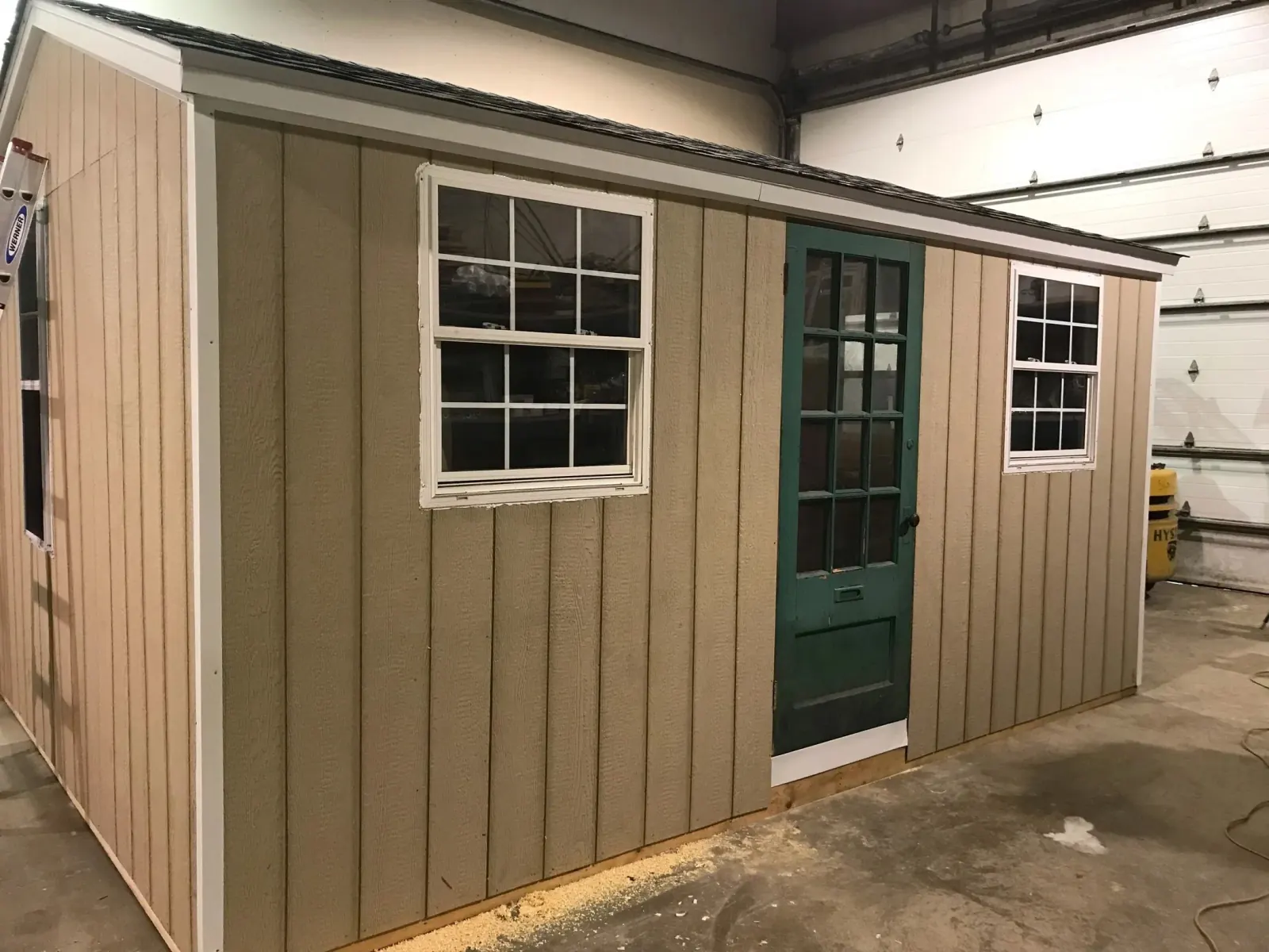 Shed under construction in the workshop, fitted with two white sash windows and a salvaged green panelled door